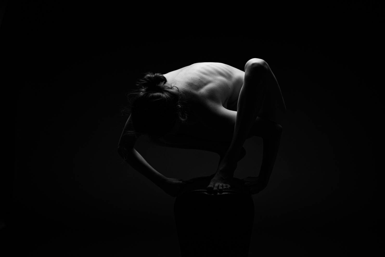 a naked woman leaning on a stool in the dark