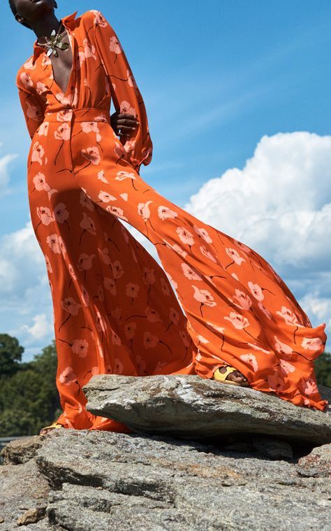 a woman in an orange dress standing on a rock