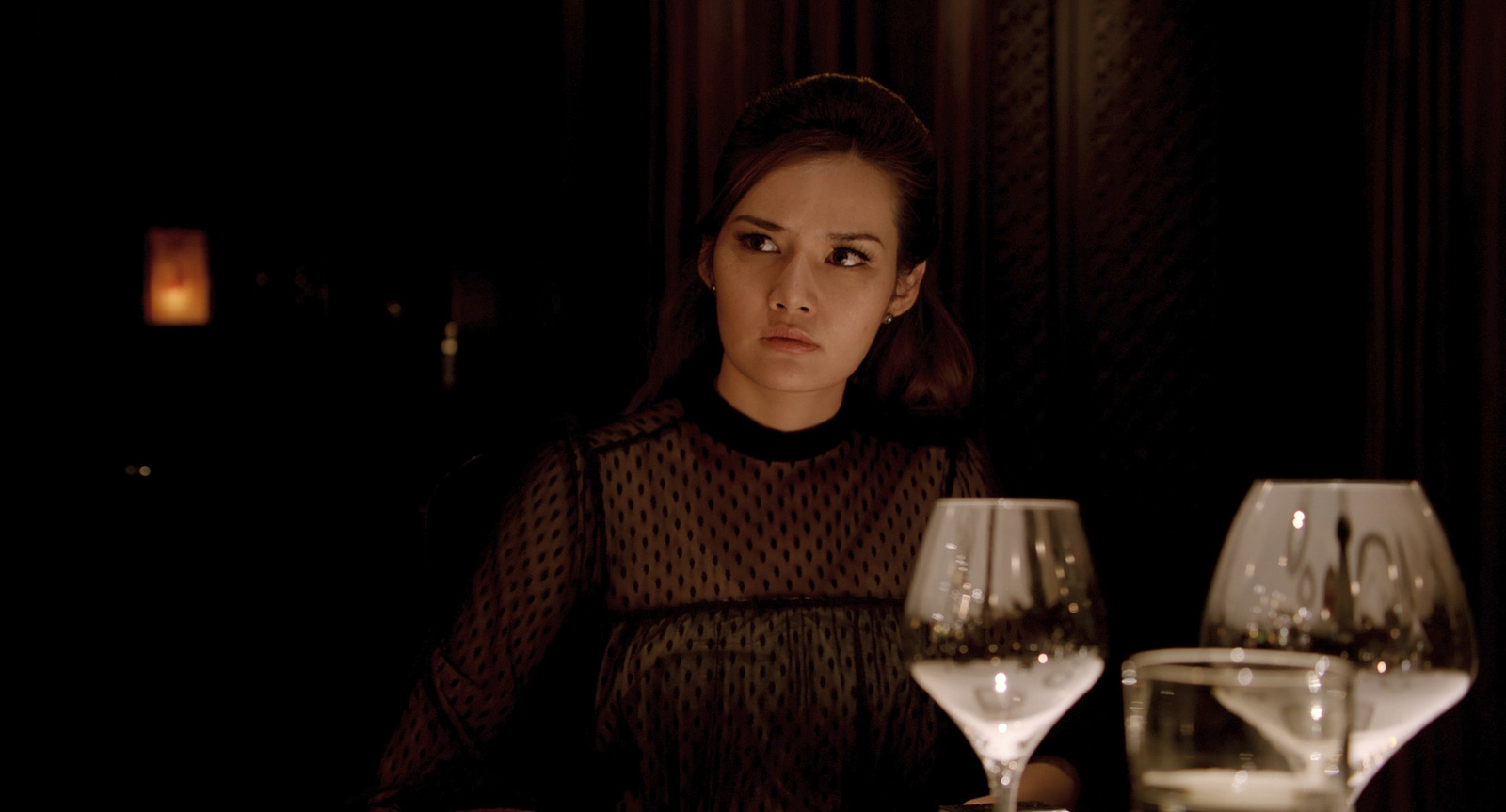 a woman sitting at a table with two wine glasses