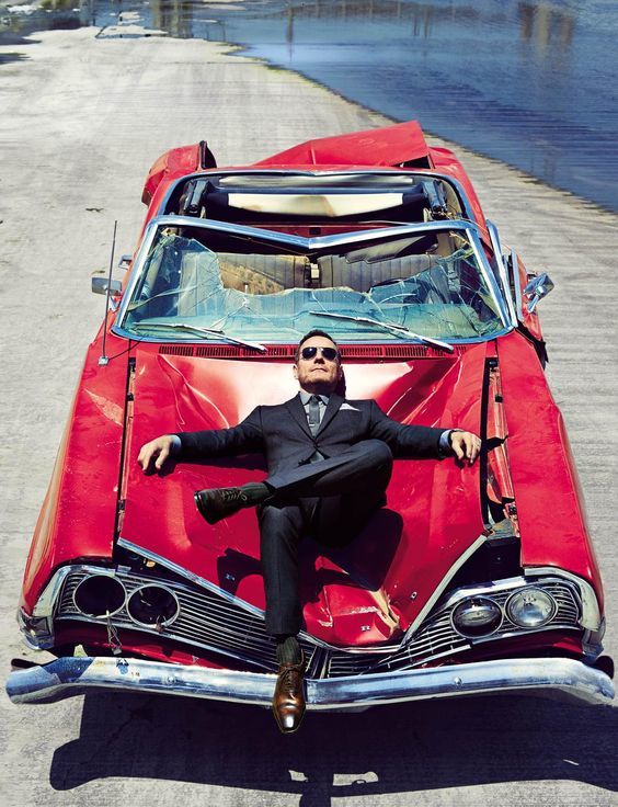 a man in a suit sitting on top of a red car