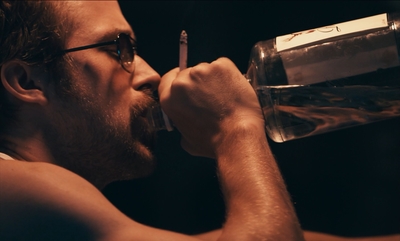 a man drinking water from a glass with a cigarette in his mouth