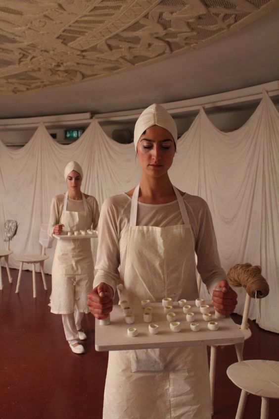 a woman in a white apron holding a tray of cupcakes