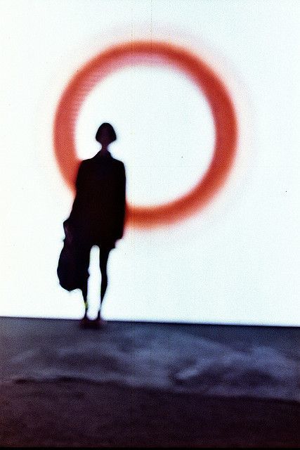 a silhouette of a person walking past a wall with a red circle on it