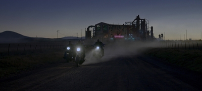 a couple of people riding motorcycles down a dirt road