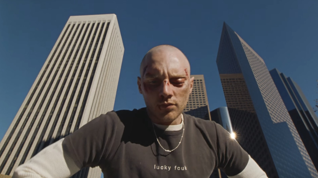 a bald man standing in front of tall buildings