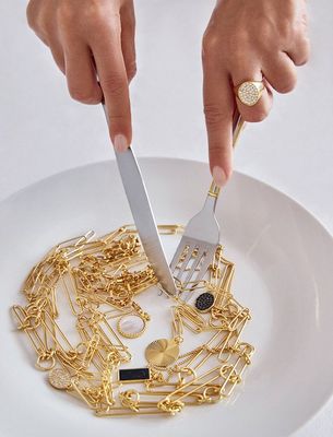 a person holding a knife and fork over a plate of gold chains