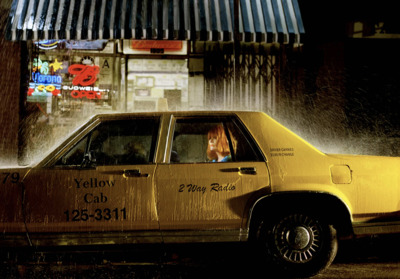 a yellow taxi cab driving down a rain soaked street