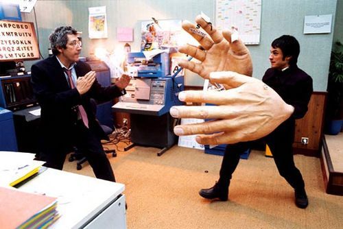 a man in a suit and tie standing next to a giant hand