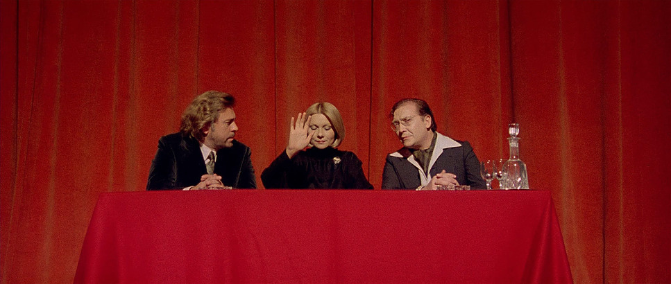 three people sitting at a table in front of a red curtain