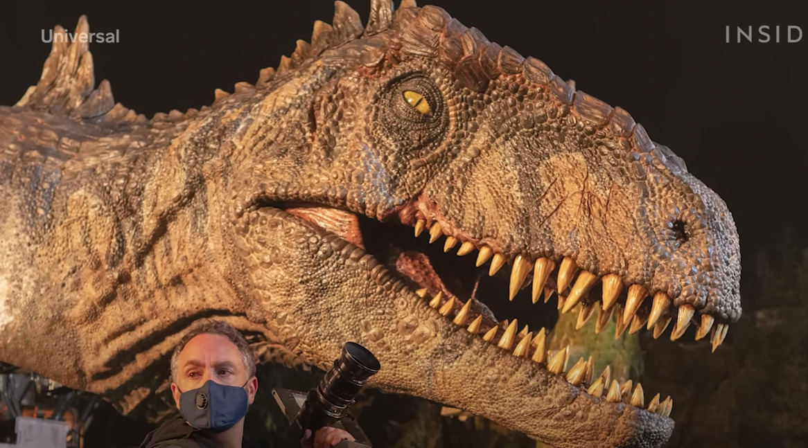 a man wearing a face mask standing next to a dinosaur