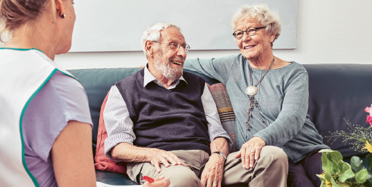 an older man and woman sitting on a couch talking to each other