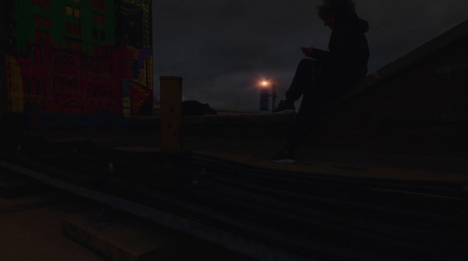 a person sitting on a ledge at night using a cell phone