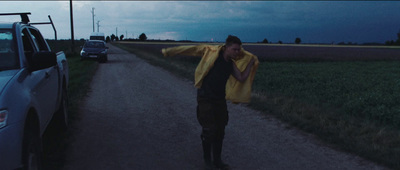 a man walking down a dirt road next to a car
