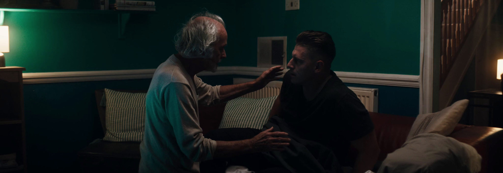 a man is shaving another man's face in a dark room