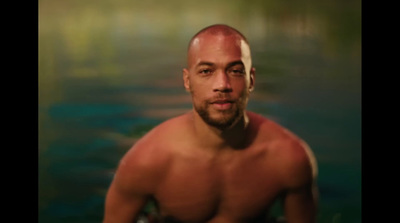 a man with a bald head standing in front of a body of water