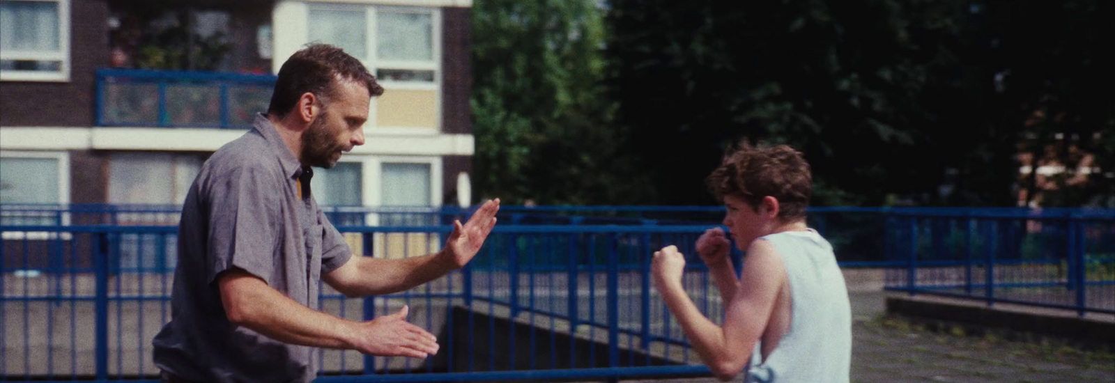 a man standing next to a little boy in front of a blue fence