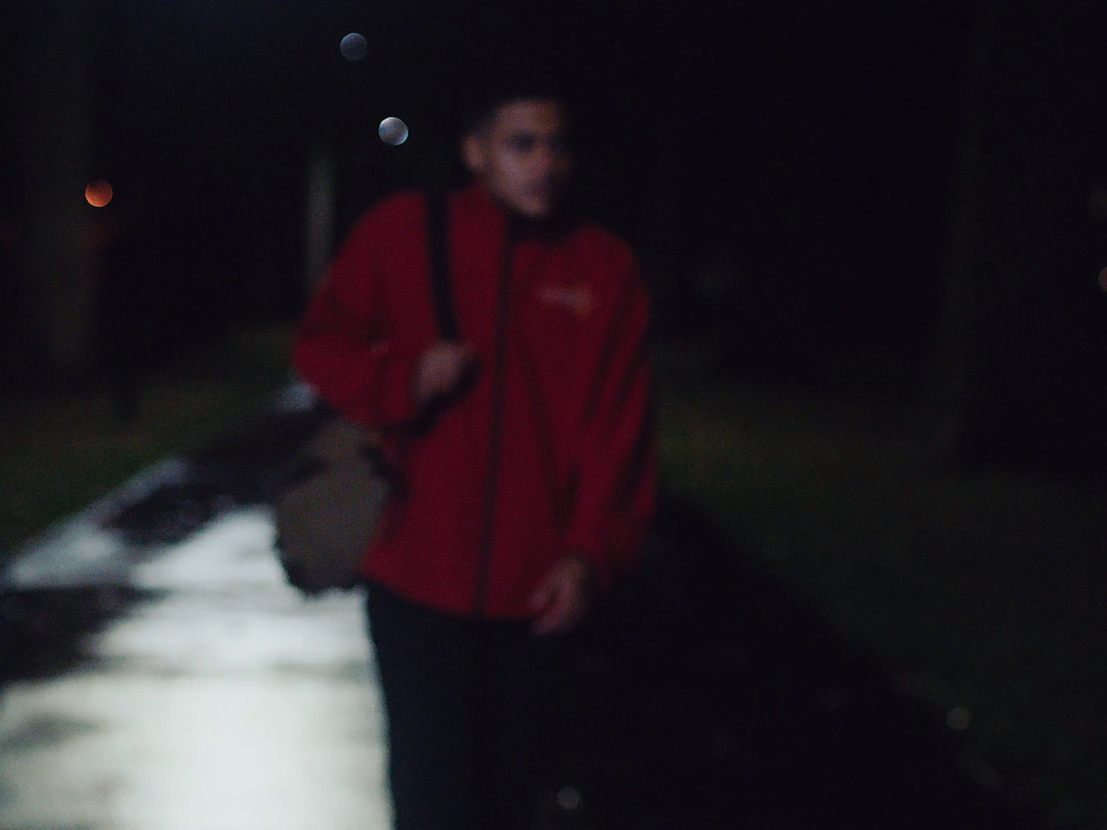 a man in a red jacket walking down a street at night