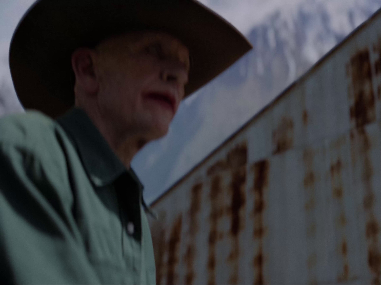 a man wearing a cowboy hat standing in front of a rusted building