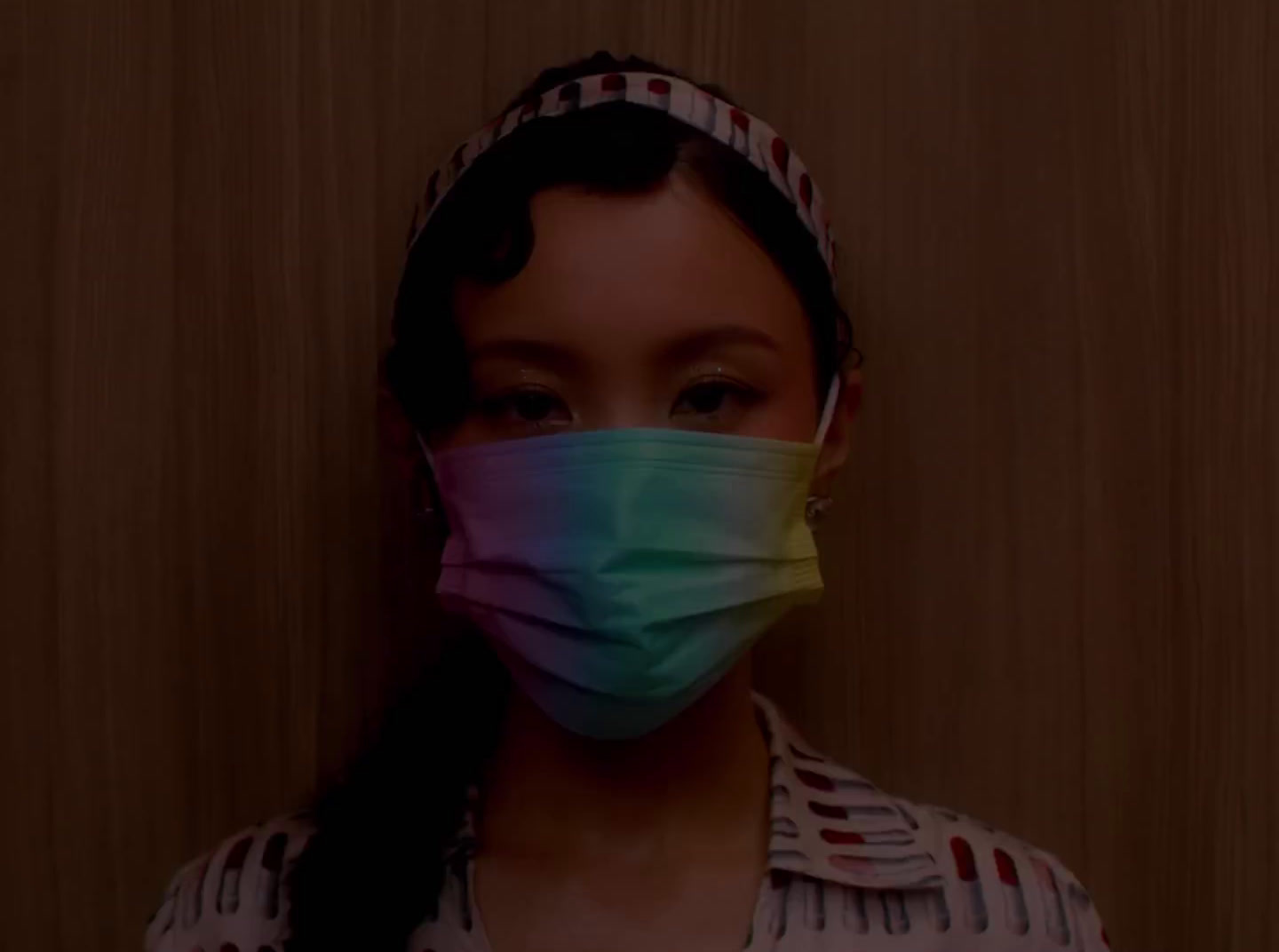 a woman wearing a face mask in front of a wooden wall