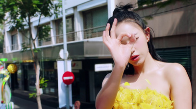 a woman in a yellow dress holding her hand up to her face