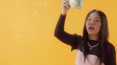 a young woman holding up a camera in front of a yellow wall