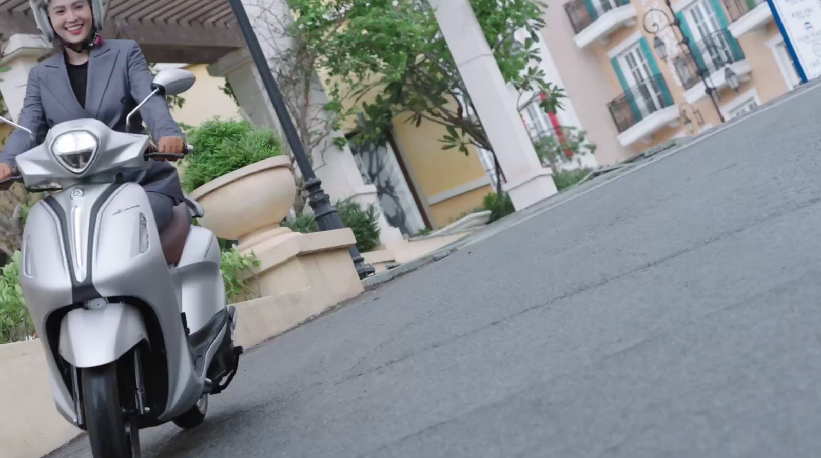 a woman riding a silver scooter down a street