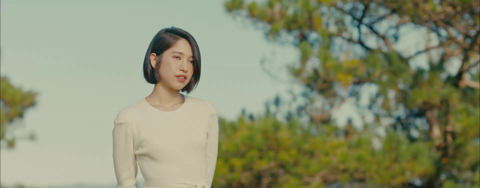 a woman in a white dress standing in front of trees