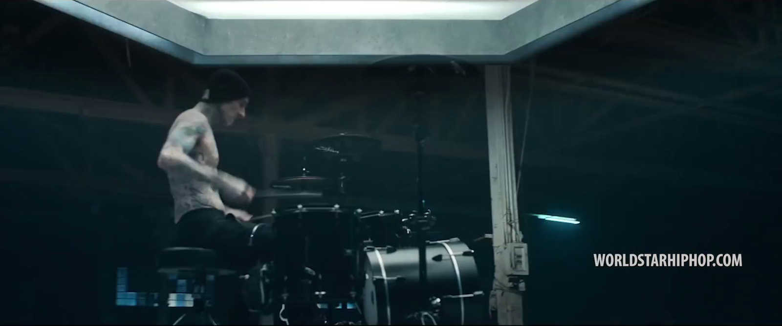 a shirtless man playing drums in a dark room