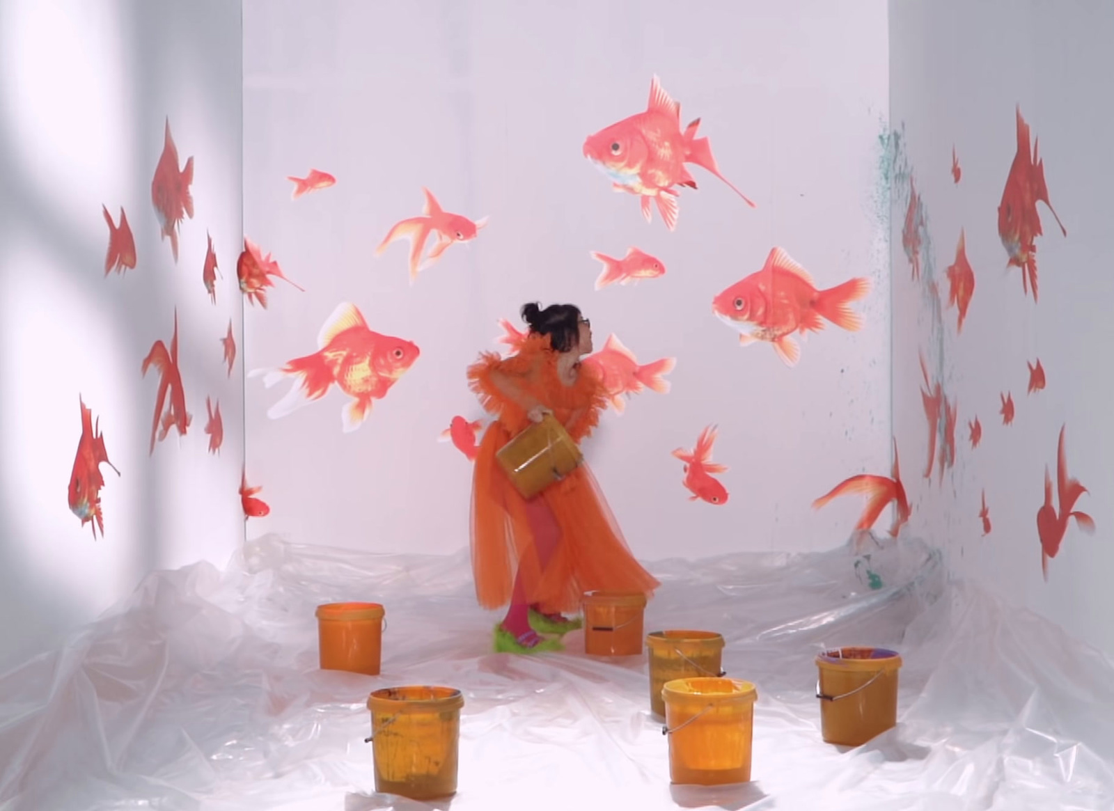 a woman in an orange dress standing in a room with fish on the walls