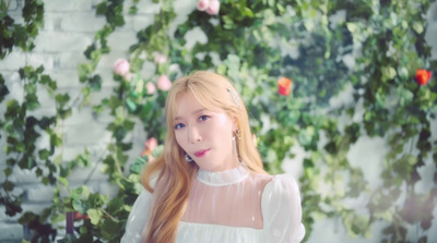 a woman with long hair standing in front of a wall of flowers