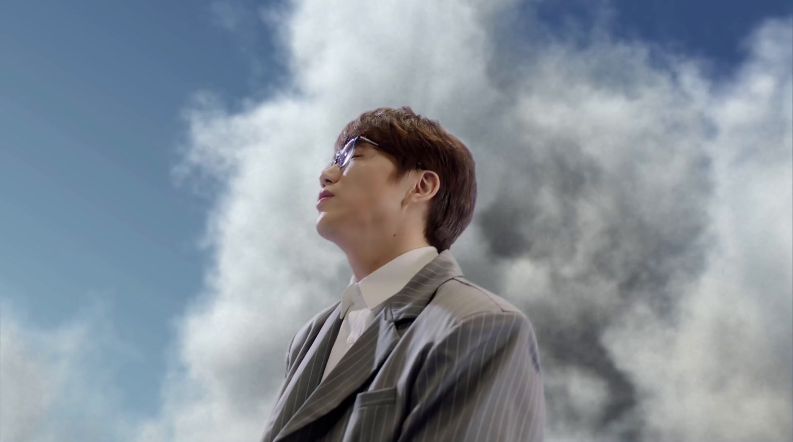 a man in a suit and tie standing in front of a cloudy sky