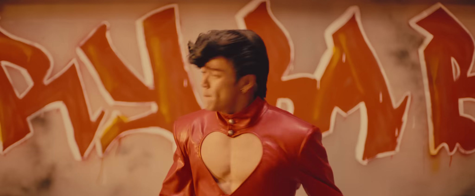 a man in a red leather outfit standing in front of a graffiti wall