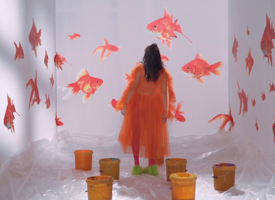 a girl in an orange dress standing in a room with goldfish on the walls