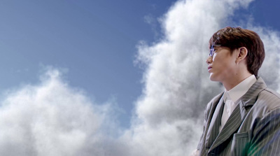 a man in a suit and tie standing in front of clouds