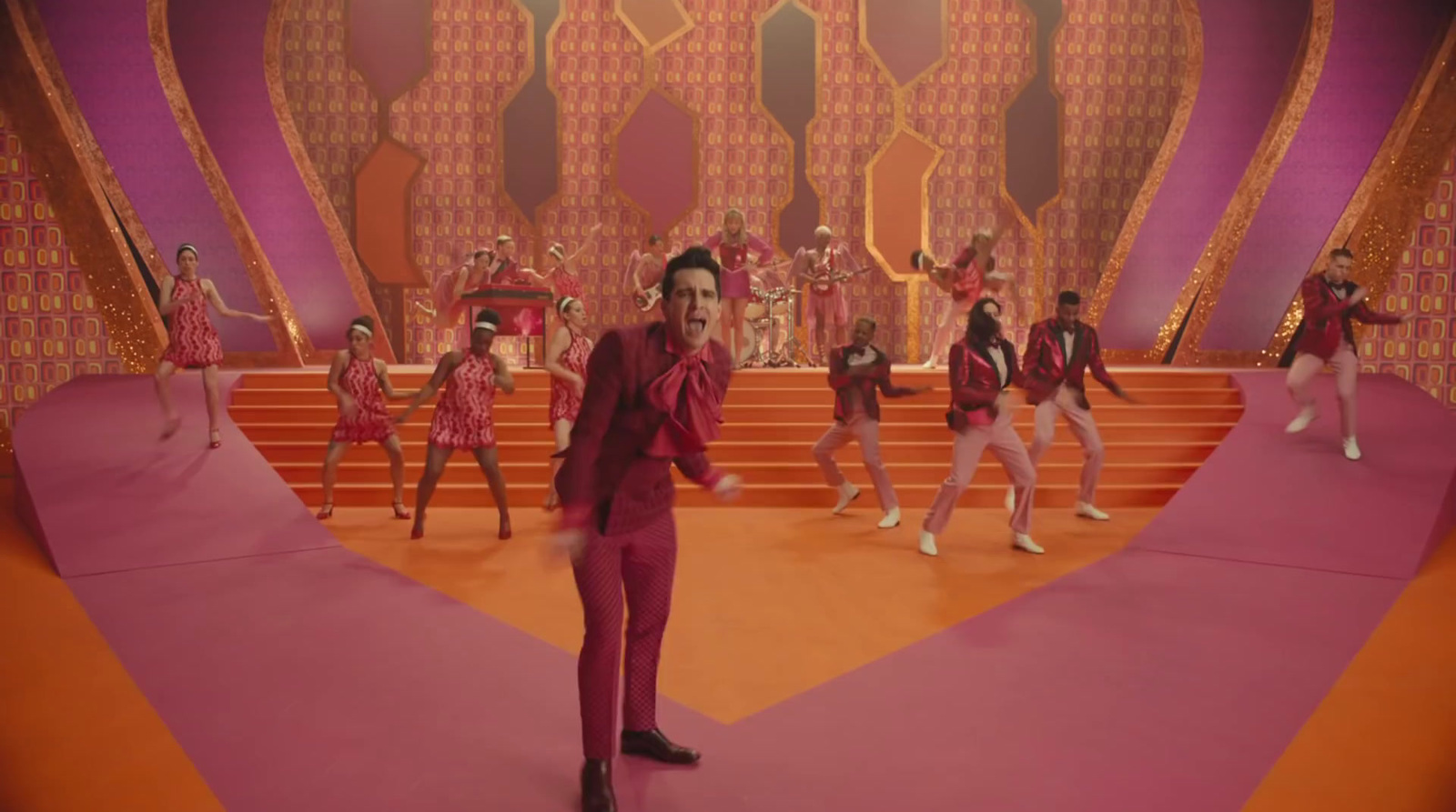 a man in a red suit standing in front of a group of dancers