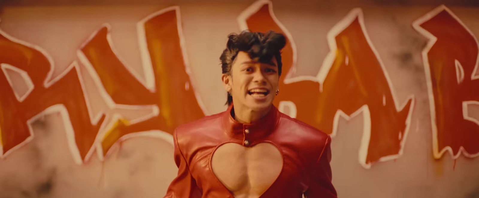 a man in a red leather outfit standing in front of a graffiti wall