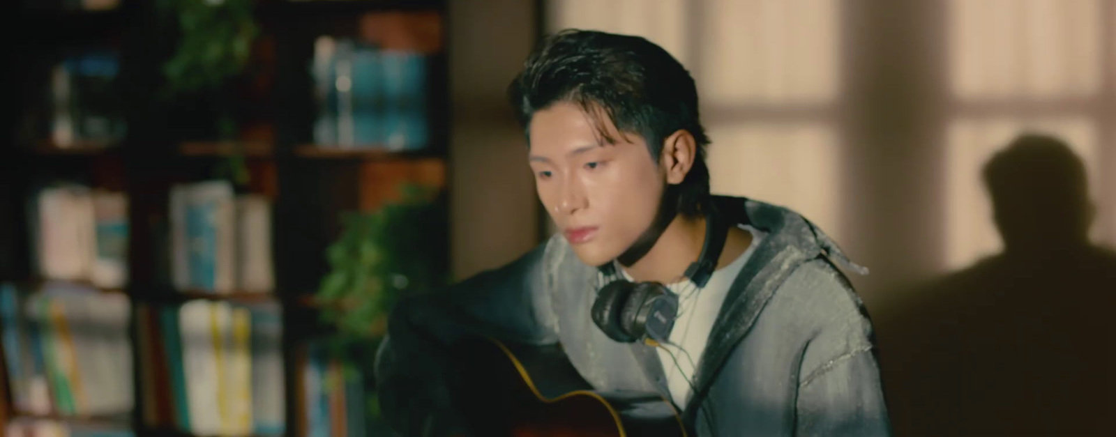 a man playing a guitar in front of a bookshelf