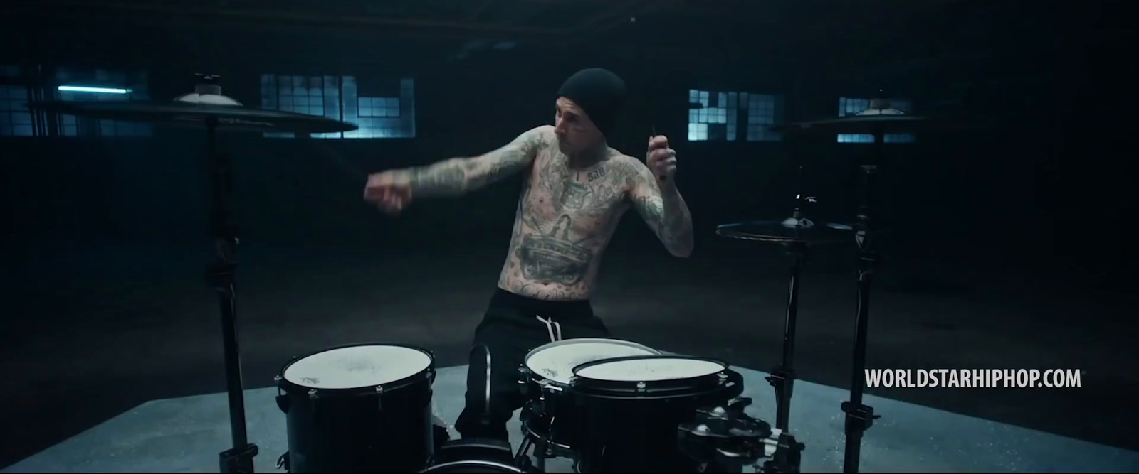 a man with tattoos playing drums in a dark room