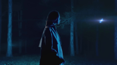 a woman standing in a dark forest at night