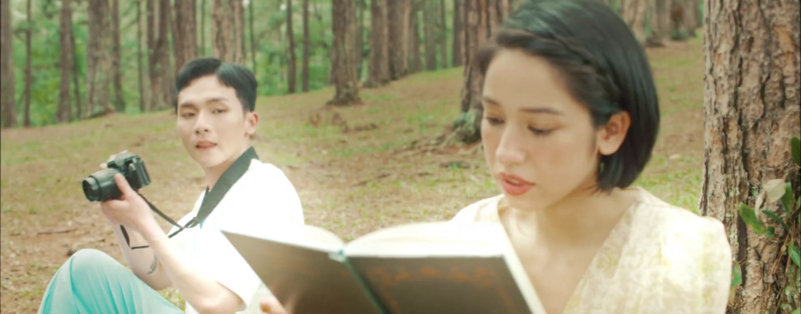 a man and a woman sitting in the woods reading a book