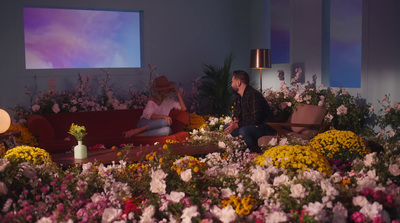 two people sitting on a couch surrounded by flowers