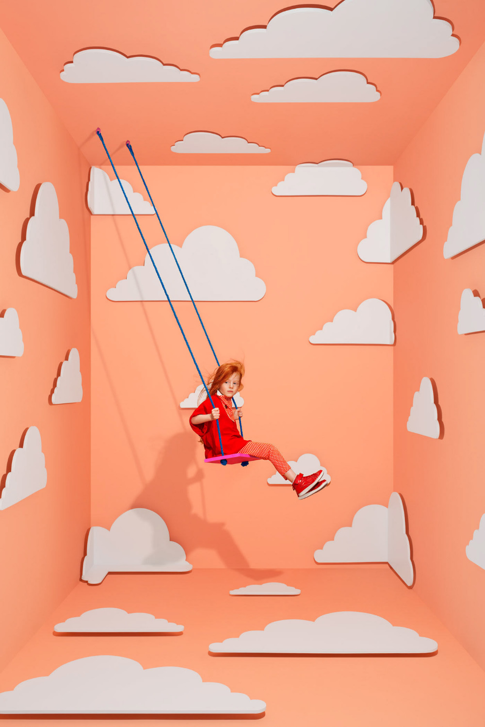 a girl is swinging on a rope in a room with clouds