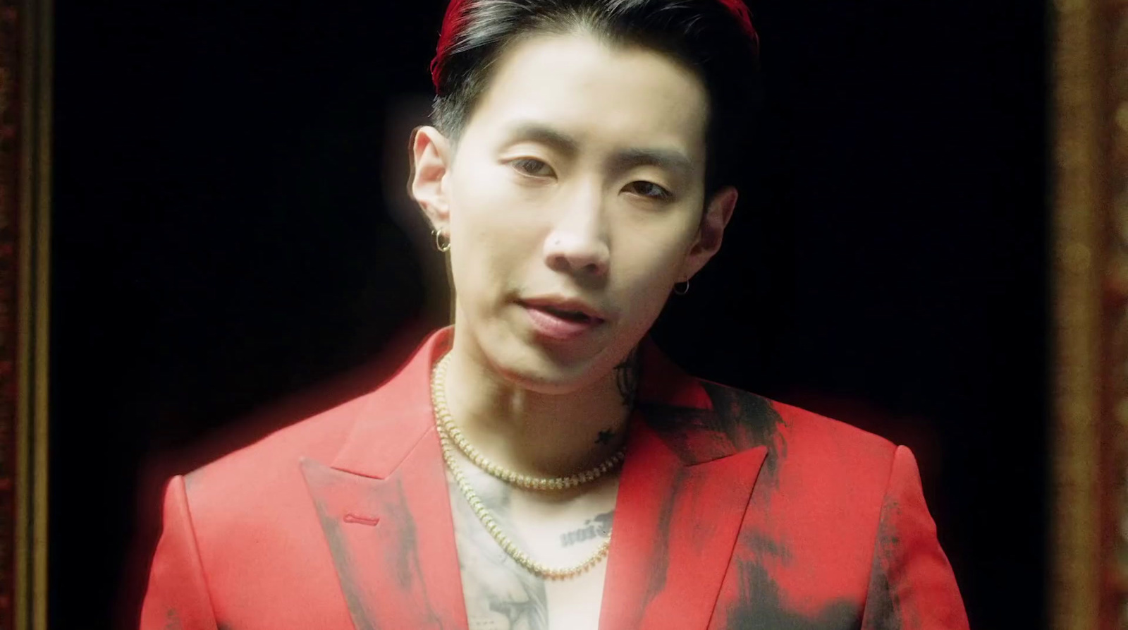 a man wearing a red jacket and pearl necklace