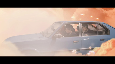 two men in a blue car driving through a cloud of smoke