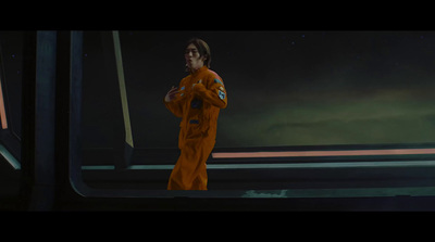 a man in an orange space suit standing in front of a window