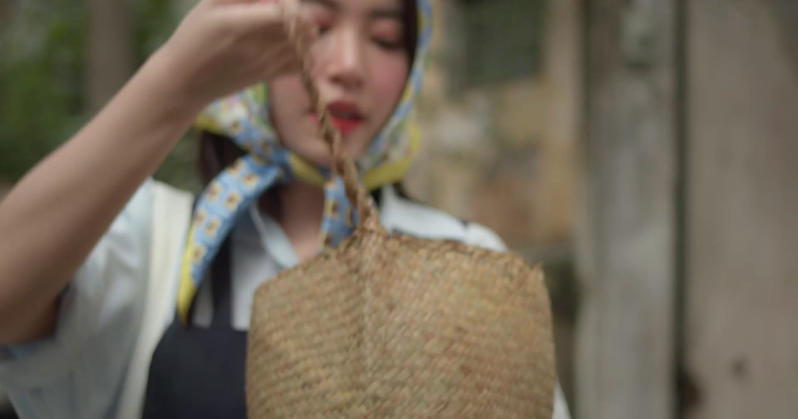 a woman holding a straw bag with a blue scarf around her neck