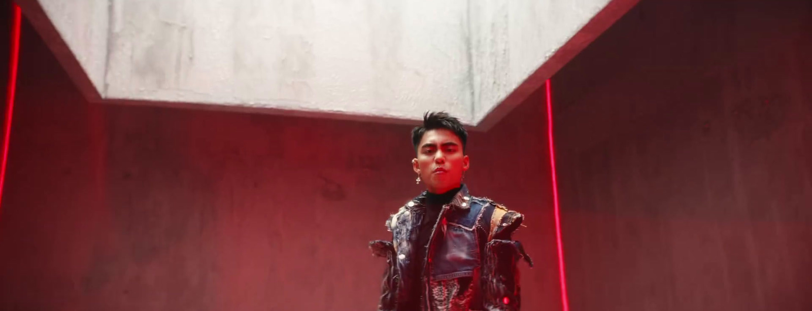 a man in a leather jacket standing in front of a red wall