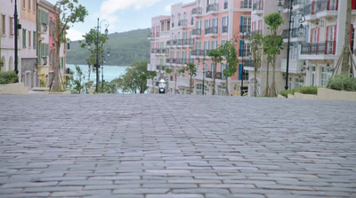 a brick road with buildings on both sides and a body of water in the distance