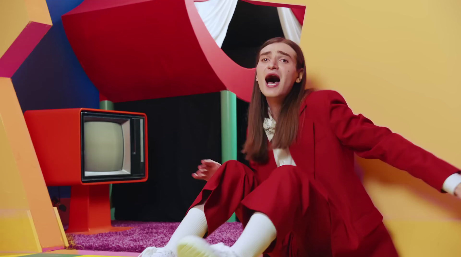 a woman in a red suit sitting on a colorful floor