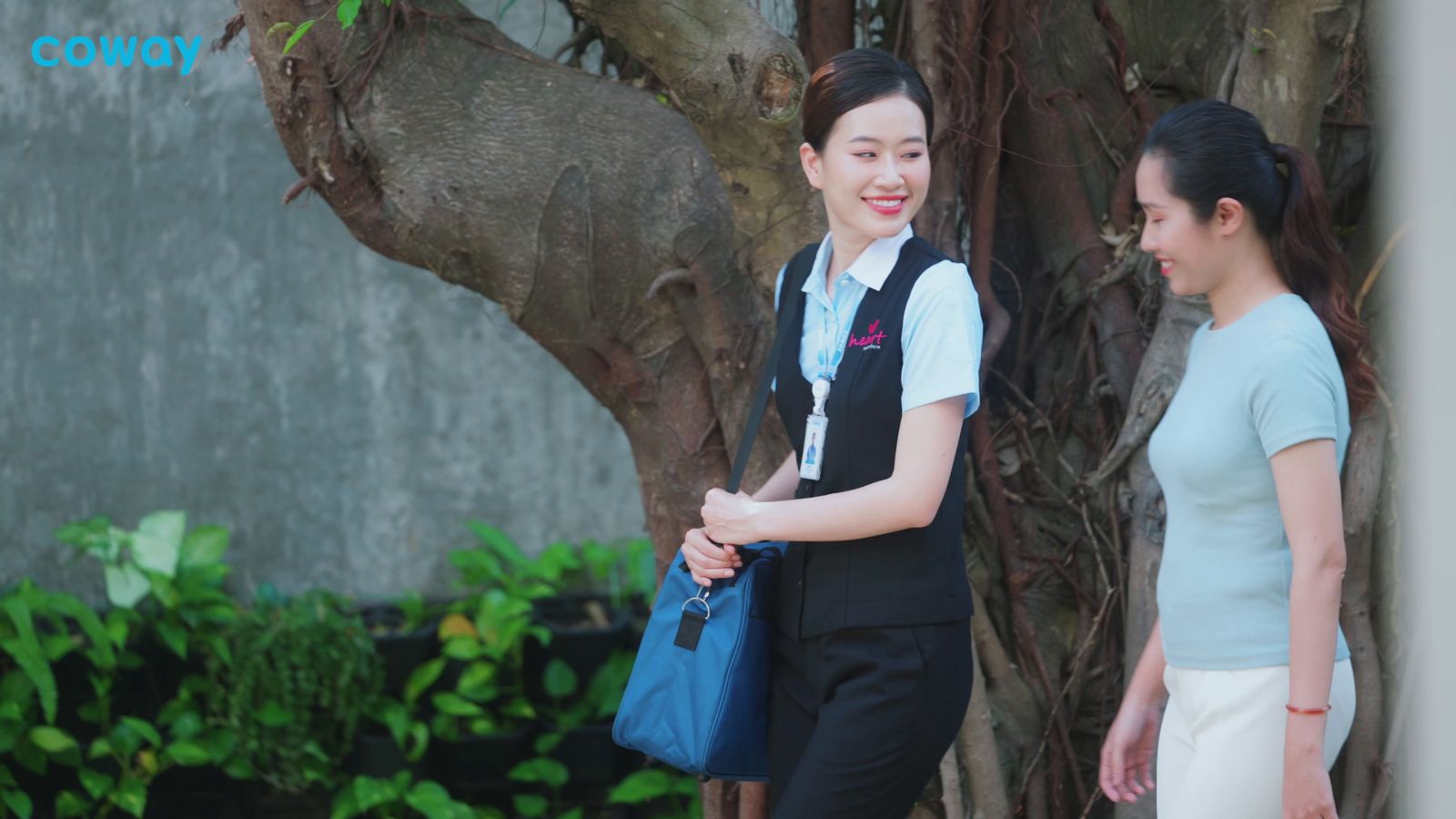 two women walking down a sidewalk next to a tree